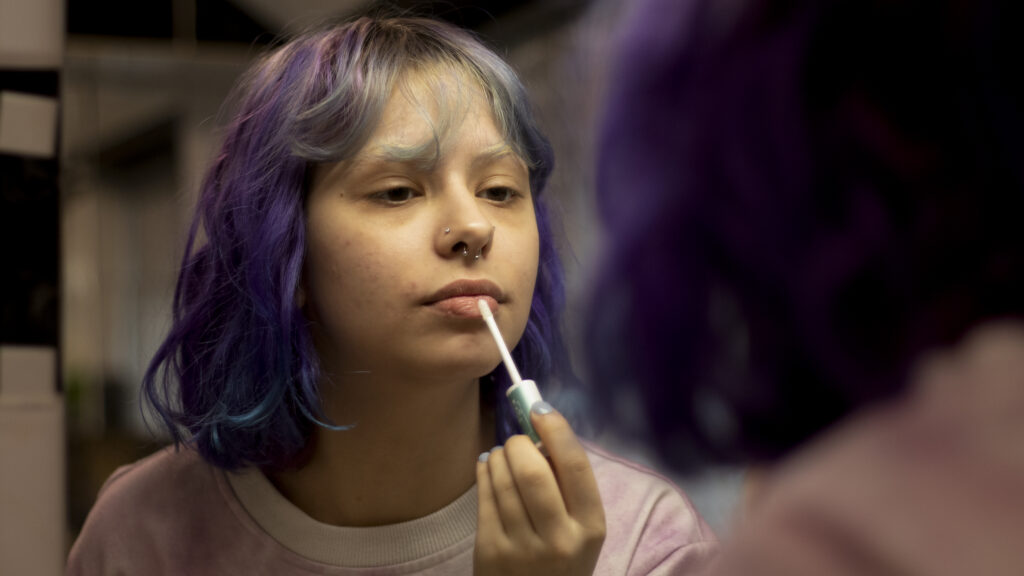 Girl with purple hair putting on lipstick