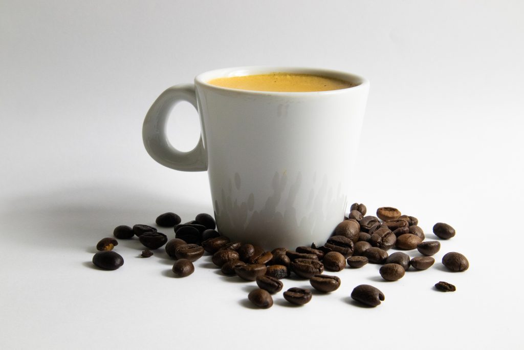 White cup filled with coffee on white background and beans in front